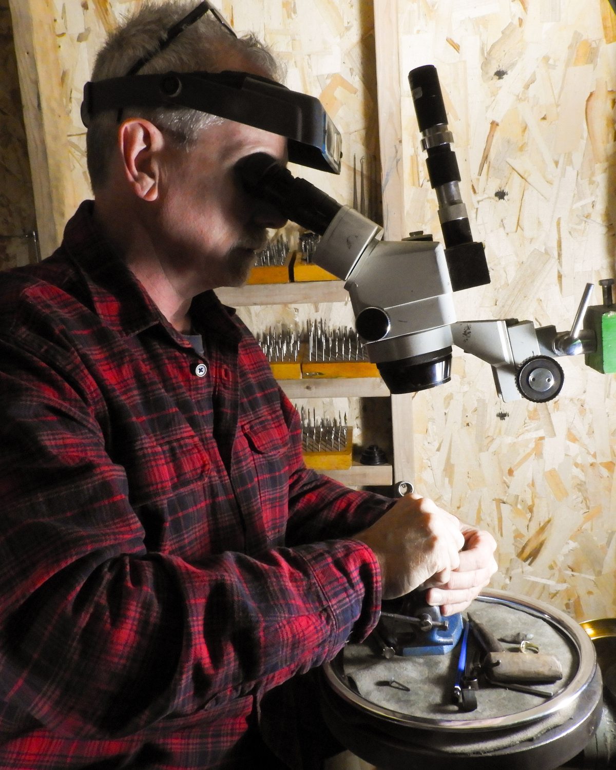Warren Smith bent over a stereo microscope, engraving a piece held in a hand vise at his workbench