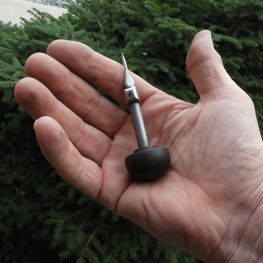 A hand holding a hand-engraving graver tool, outdoors